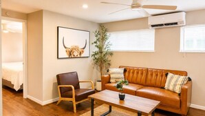 Un salon avec un canapé en cuir marron, une chaise en bois, une table basse, une plante et un tableau encadré accroché au mur.