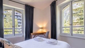 Hotellihuone, jossa on sänky, työpöytä ja kaksi ikkunaa, joissa on verhot.