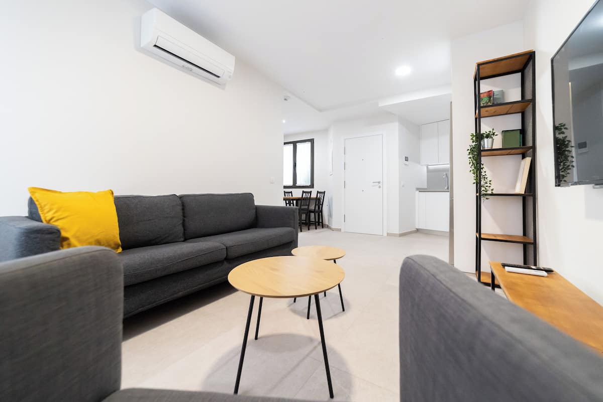 A modern living room with a grey sofa, a yellow pillow, and two wooden tables.