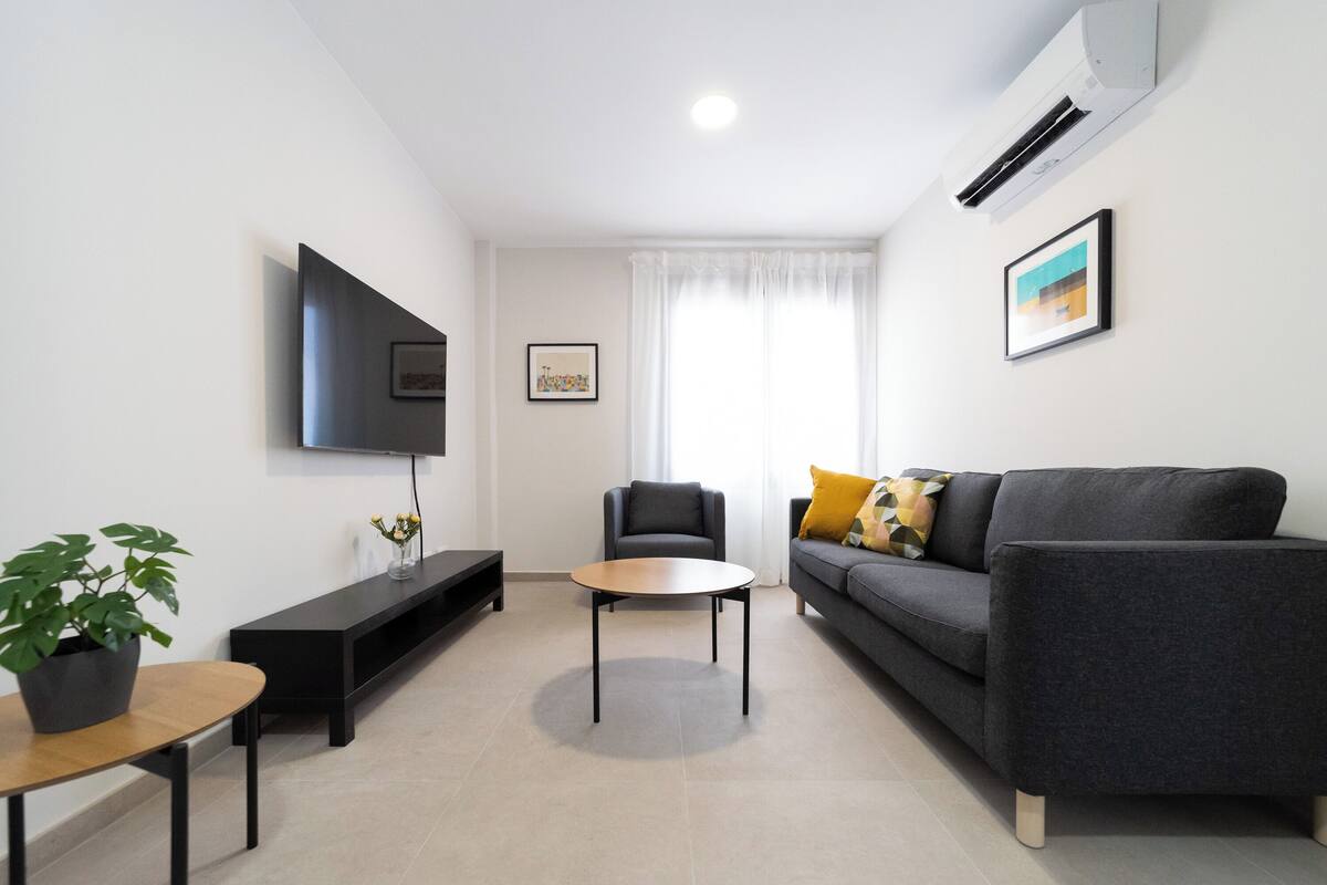 A modern living room with a flat-screen TV, a sofa, a coffee table, and a chair.