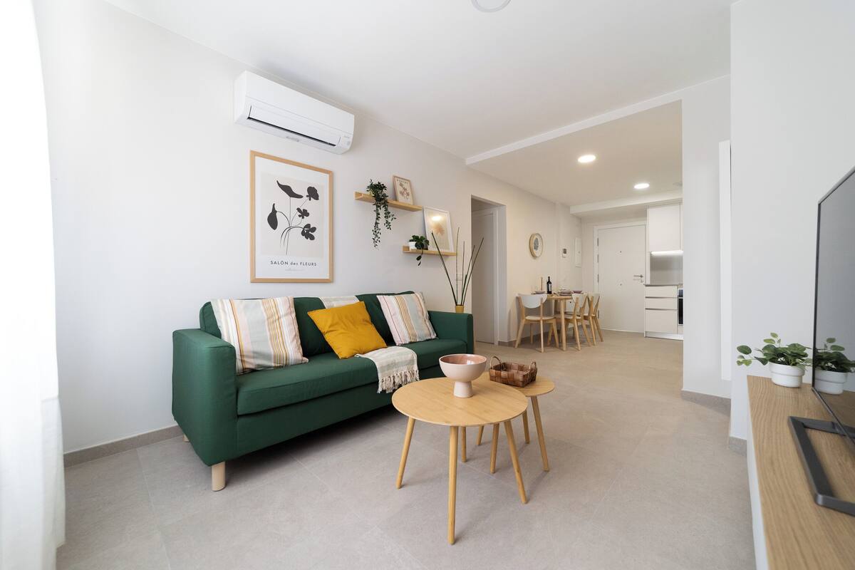 A modern living room with a green sofa, two wooden tables, and a TV on a wooden stand.