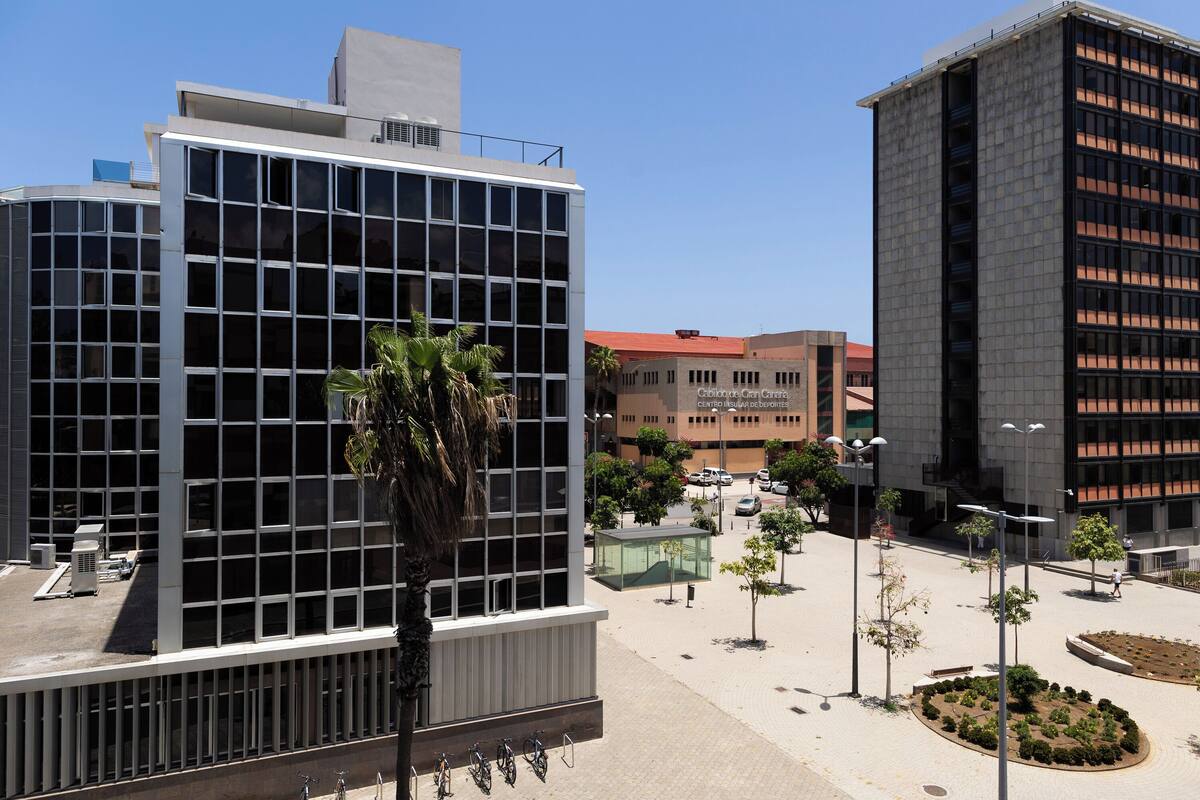 A modern building with a glass facade, a central courtyard with trees, and a bike rack.