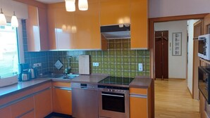 Eine Küche mit orangenen Schränken, einem Geschirrspüler, einem Backofen und Pendelleuchten.