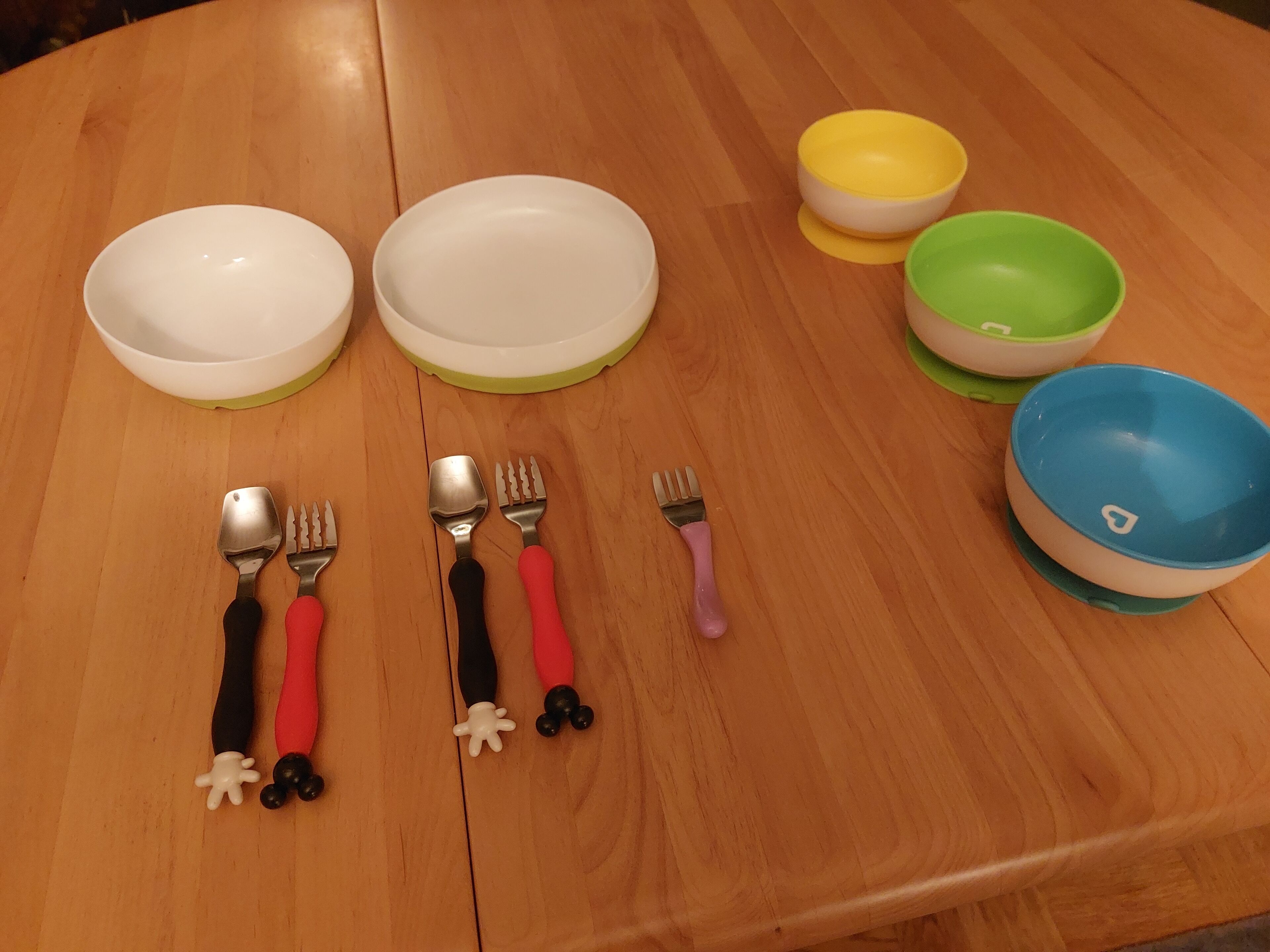 Una mesa de madera con cuatro cuencos y cuatro tenedores, cada uno con mangos de colores diferentes.