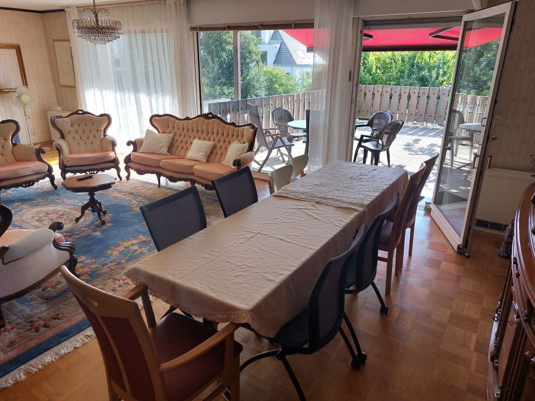 Un'area pranzo con un tavolo apparecchiato per quattro persone, circondato da sedie. Si intravede un balcone con posti a sedere all'aperto attraverso le porte vetrate.
