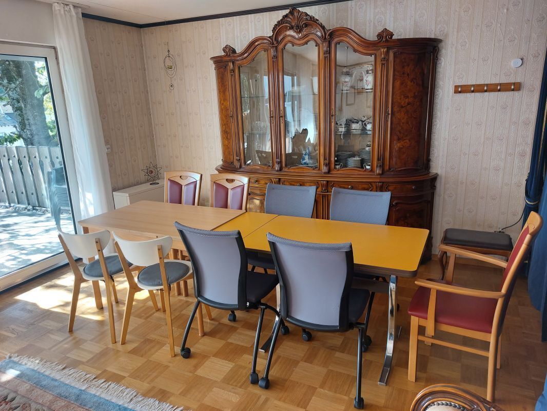 A dining area with a wooden table and chairs, a large cabinet with glass doors, and a view through a sliding glass door.