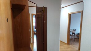 Ein Flur mit Holzboden, einer Tür mit Messinggriff und einem sichtbaren Bett im Hintergrund.