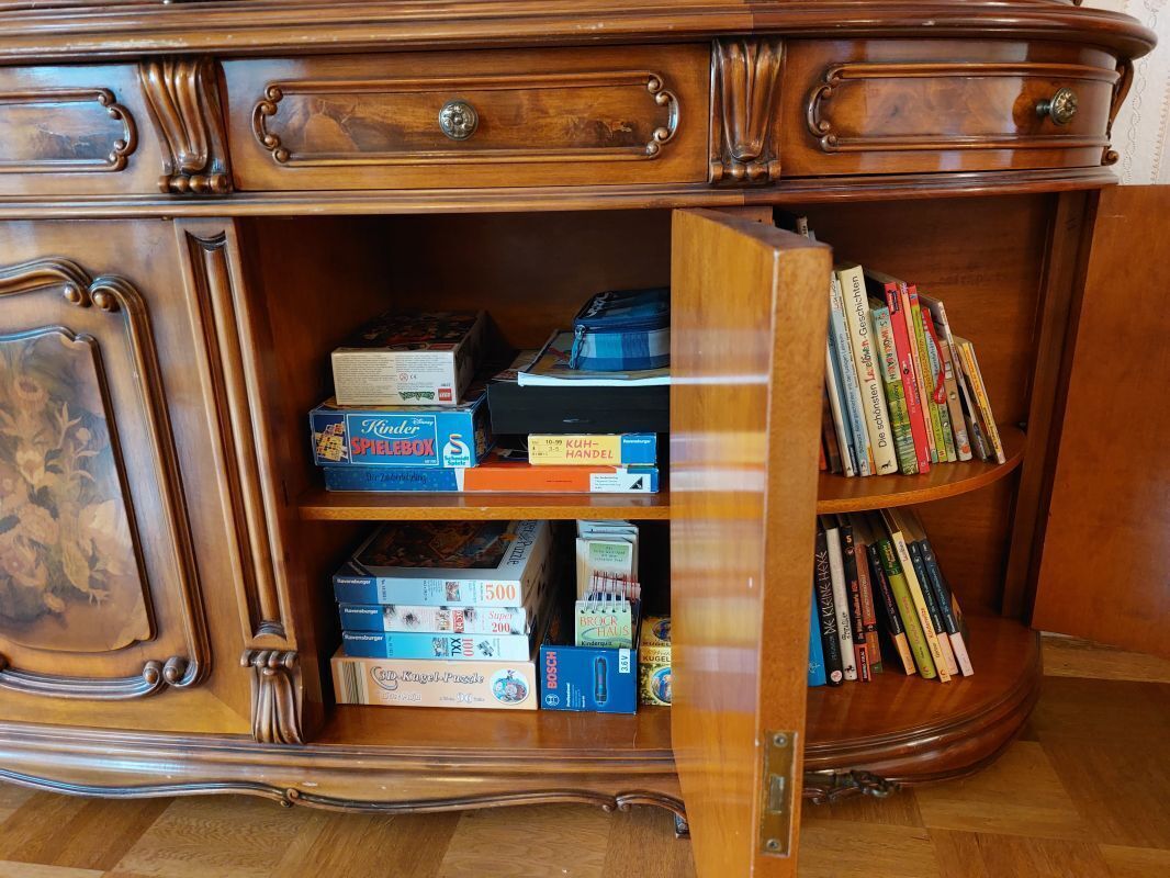 A wooden cabinet with multiple compartments, some containing books and others with board games.