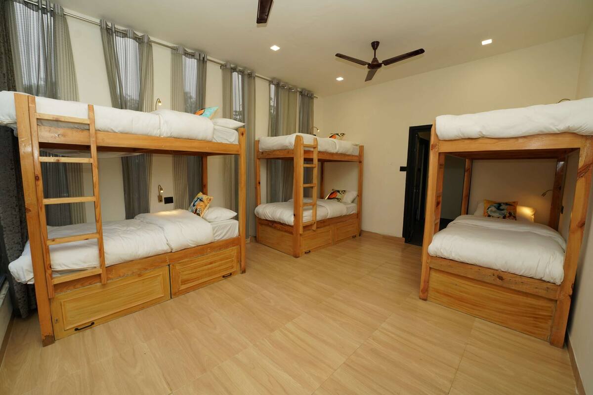 Una habitación con tres literas, piso de madera y un ventilador de techo.