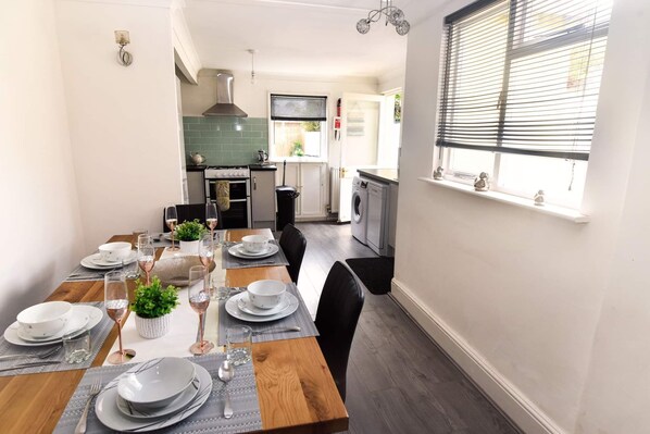 Enjoy a meal in this modern kitchen and dining area, featuring a stainless steel range, green backsplash, and wooden table.