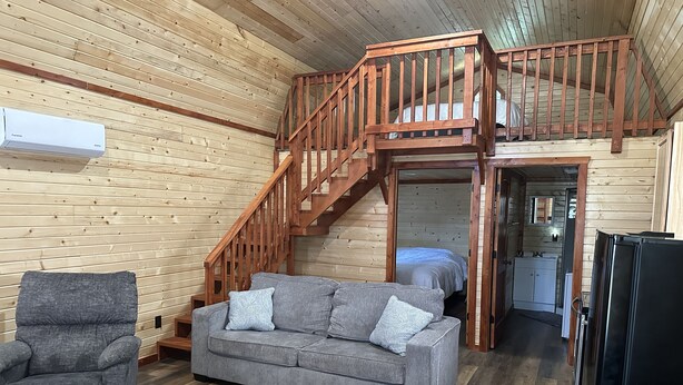 A cozy cabin interior with a wooden staircase, a sofa, a chair, and a refrigerator. - Tan cabin close to University of Central Missouri and Whiteman AF Base  (Warrensburg)