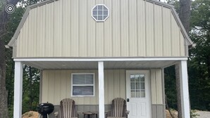 A small, single-story building with a porch, two chairs, a table, and a grill. - Tan cabin close to University of Central Missouri and Whiteman AF Base  (Warrensburg)