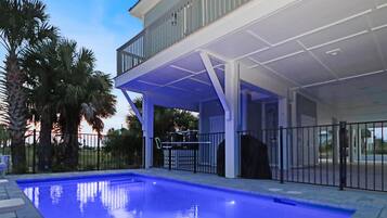 A swimming pool with a covered patio area, surrounded by palm trees and a fence.