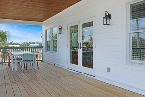 Une véranda couverte avec une terrasse en bois, une table et des chaises, et une porte vitrée à mécanisme coulissant.