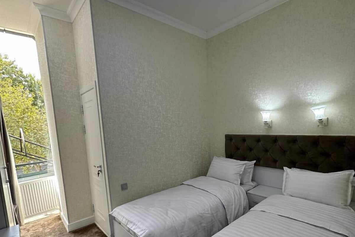 A hotel room with two beds, a small desk, and a balcony with a view.