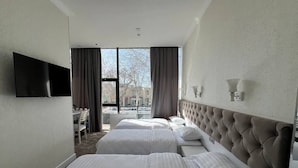 A hotel room with two beds, a flat-screen TV mounted on the wall, and a view of the city through large windows. - Hotel Panorama Samarkand (Samarkand)