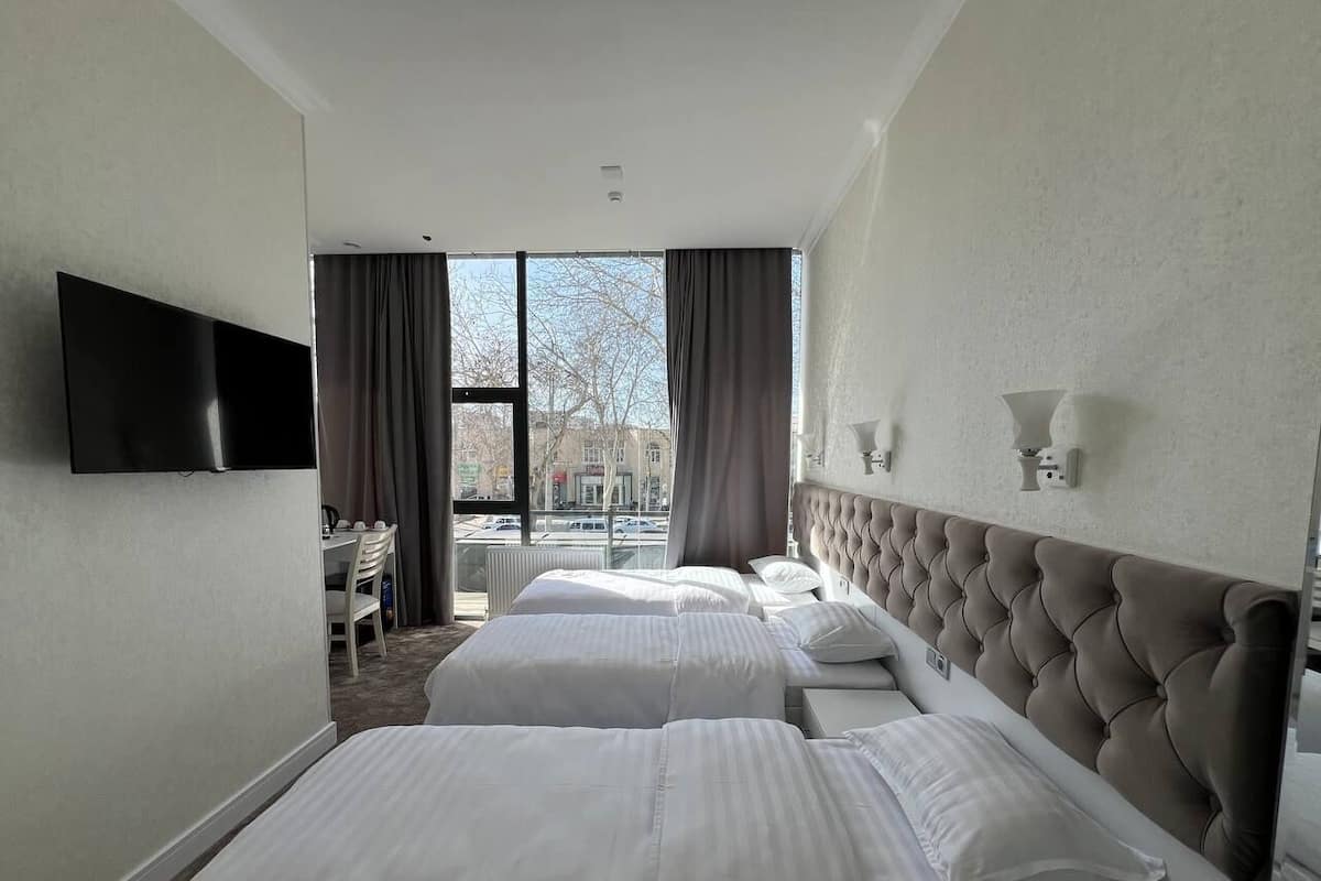 A hotel room with two beds, a flat-screen TV mounted on the wall, and a view of the city through large windows.