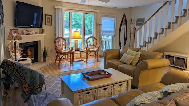 A living room with a fireplace, a television, wicker chairs, a sofa, and a staircase. - Dog-Friendly 3BR Townhome with All Seasons Room – Bayberry Woods (Bethany Beach)