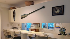 A modern kitchen with a central island, bar stools, a hanging paddle, and a framed picture of a ship. - Dog-Friendly 3BR Townhome with All Seasons Room – Bayberry Woods (Bethany Beach)