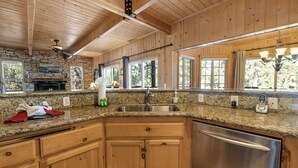 Une cuisine dotée de plans de travail en granit, de meubles en bois, d’un lave-vaisselle en acier inoxydable et d’une cheminée en pierre.
