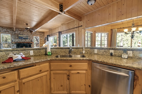 A kitchen with granite countertops, wooden cabinets, a stainless steel dishwasher, and a stone fireplace. - SPACIOUS LODGE in Fox Farm, 13 people, with fun game room & a private hot tub (Big Bear Lake)