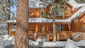 Une cabane en rondins à deux étages, dotée d’un porche à l’avant, entourée de neige et d’arbres.