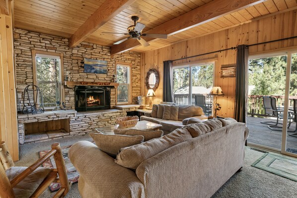 A cozy cabin interior with a stone fireplace, wooden ceiling, and a large sofa.