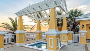 A pool area with a pergola, palm trees, and a yellow building. - Beach Haven-Spacious 3BR-3BA Pet Friendly (Gulf Shores)