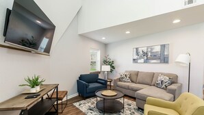 A modern living room with a flat-screen TV, a sofa, a blue armchair, a yellow armchair, a coffee table, and a small table with a plant.
