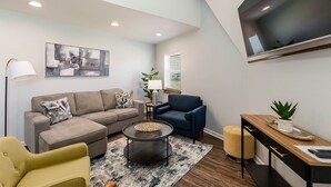 A modern living room with a sofa, armchair, coffee table, and a TV mounted on the wall. - Dynasty Dome 901 - Book for Football Season! (Tuscaloosa)