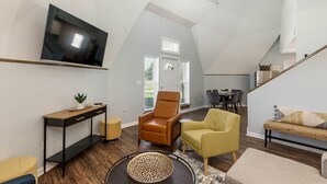 A spacious living area with a high ceiling, a television mounted on the wall, a brown leather chair, a yellow armchair, and a wicker sofa. - Dynasty Dome 901 - Book for Football Season! (Tuscaloosa)