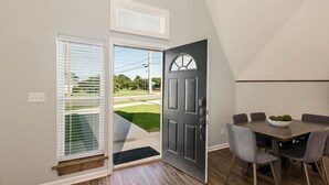 A dining area with a dark wooden table and grey chairs, a grey door with a window, and a view of a green lawn and street outside. - Dynasty Dome 901 - Book for Football Season! (Tuscaloosa)