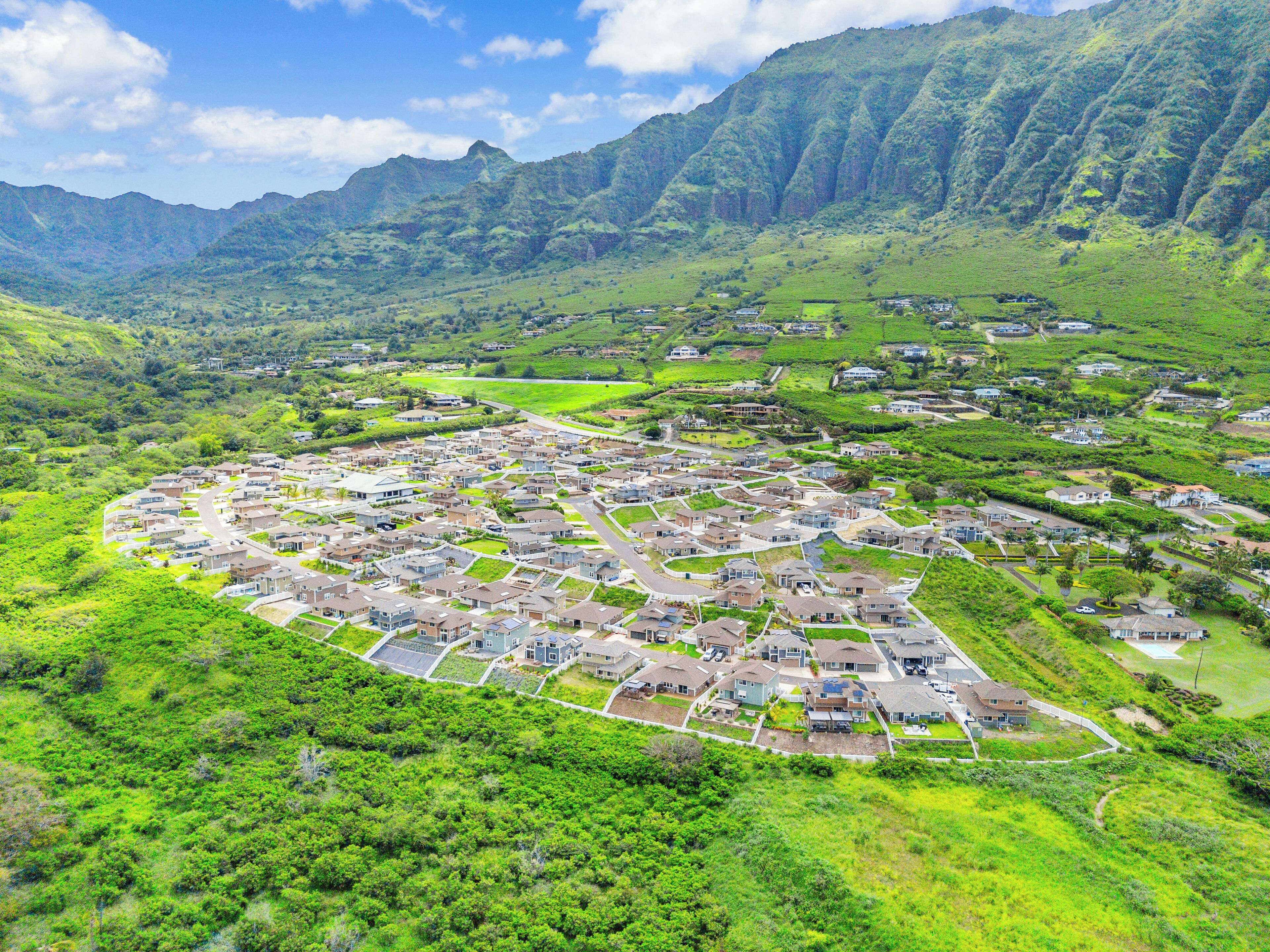 A residential area with houses arranged in a circular pattern, surrounded by lush green hills and mountains.