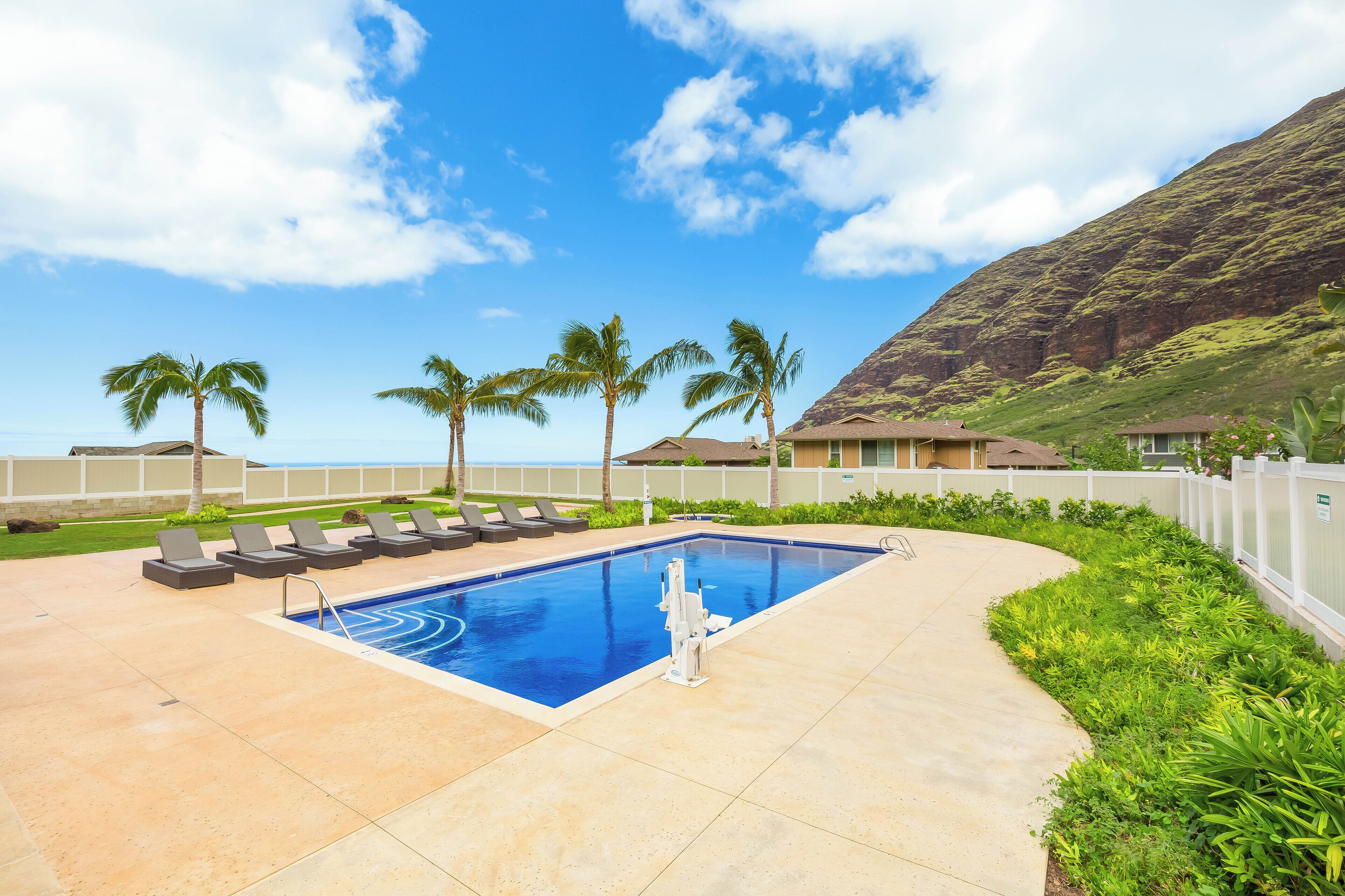 Une piscine avec des chaises longues, des palmiers et une vue sur l’océan.