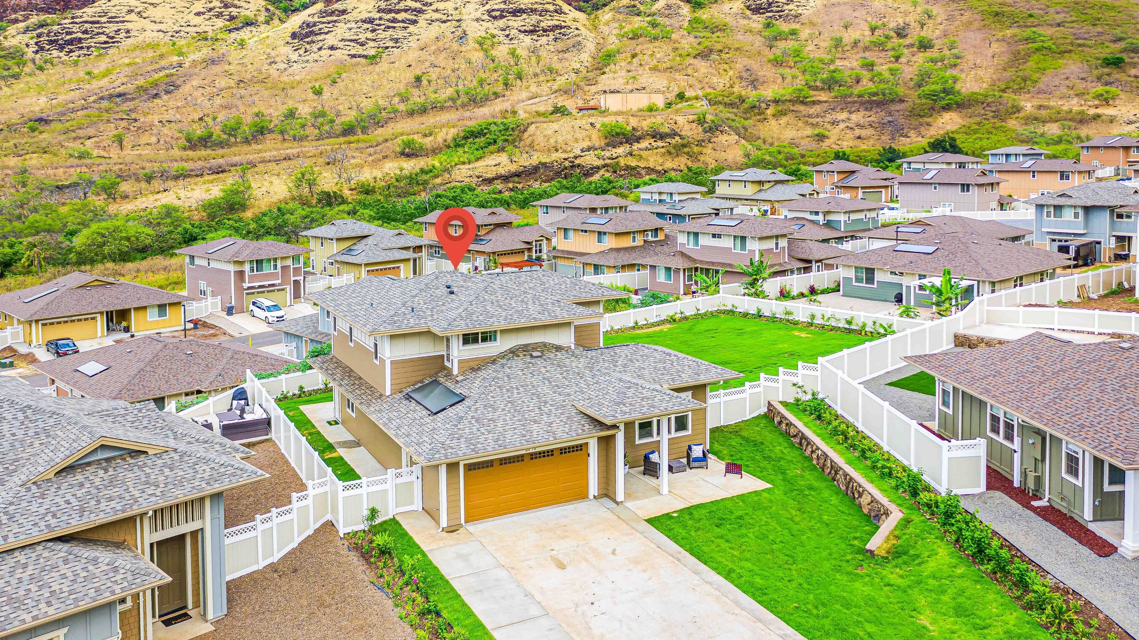 A residential area with houses featuring sloped roofs, front yards, and a hillside in the background.