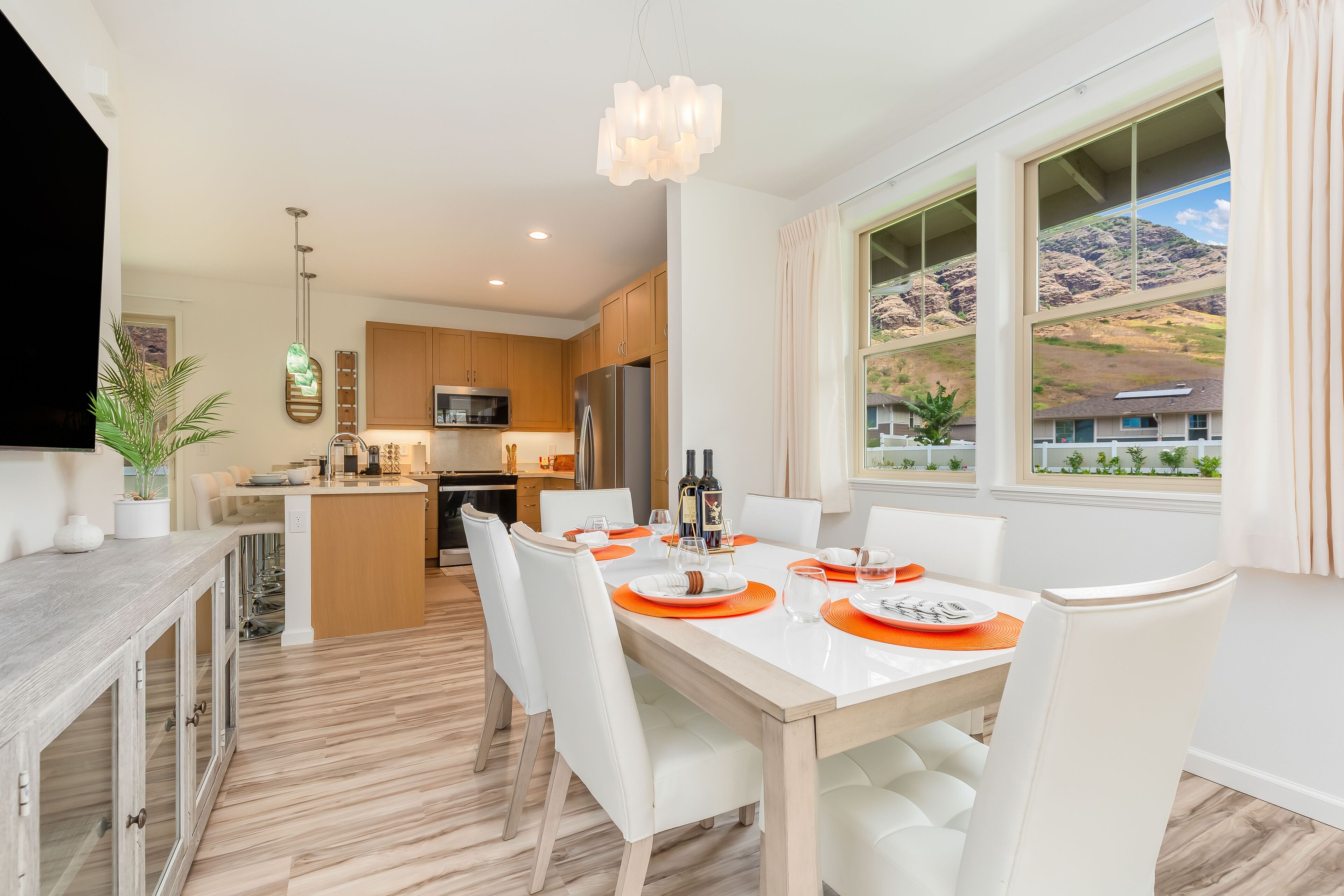 A modern kitchen with wooden cabinets, a central island, and a dining area with white chairs and orange placemats.