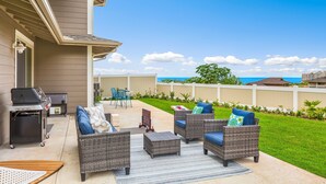 Un patio exterior con mobiliario de mimbre, una parrilla y vistas al océano.