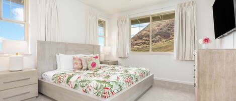 A bedroom with a bed, nightstands, a ceiling fan, a TV, and large windows with curtains.