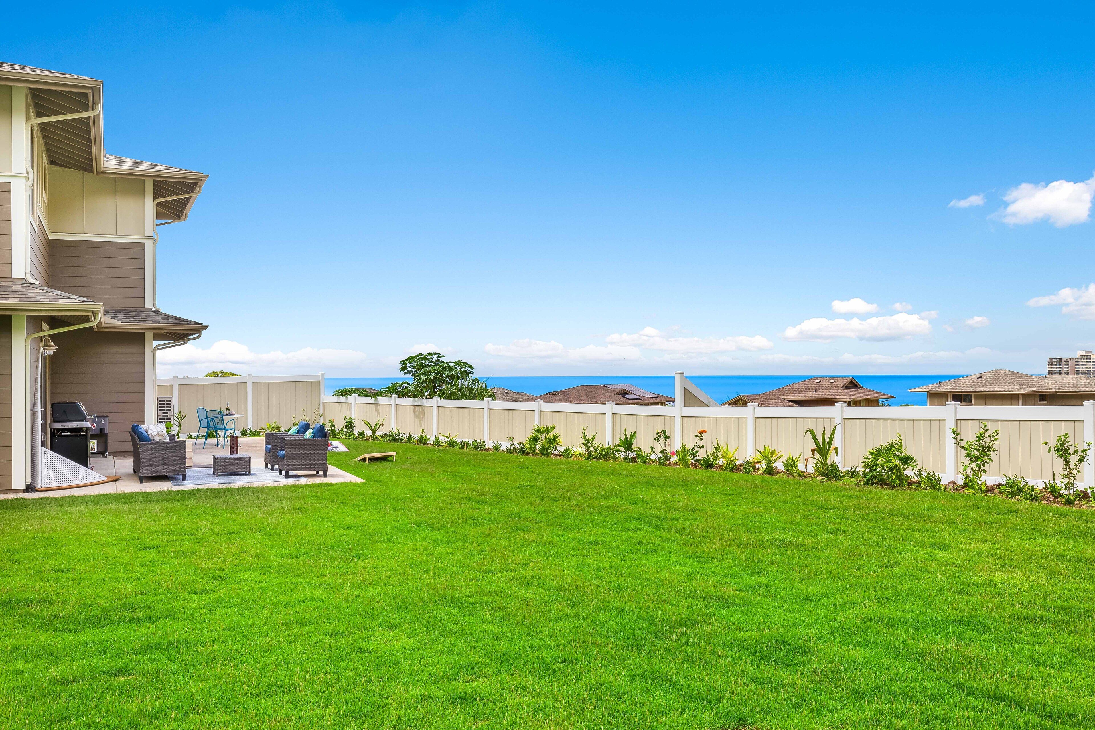 A residential backyard with a lawn, outdoor furniture, and a white fence.