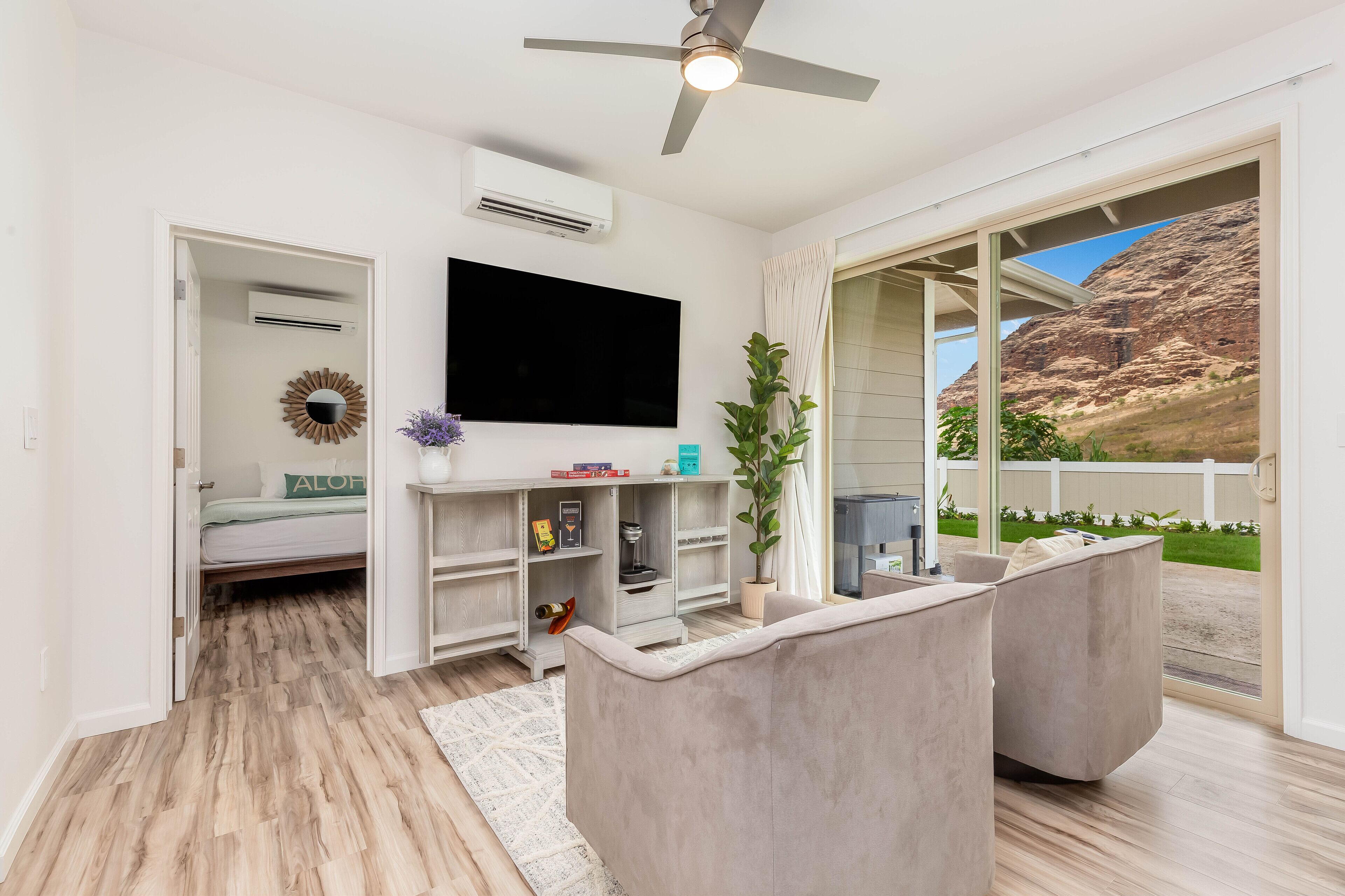 Ein modernes Wohnzimmer mit Fernseher, Einbauschränken, Deckenventilator und großem Fenster mit Blick auf eine Berglandschaft.