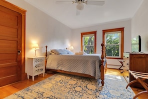 A bedroom with a wooden bed, two bedside lamps, a nightstand, a dresser, and a large window.