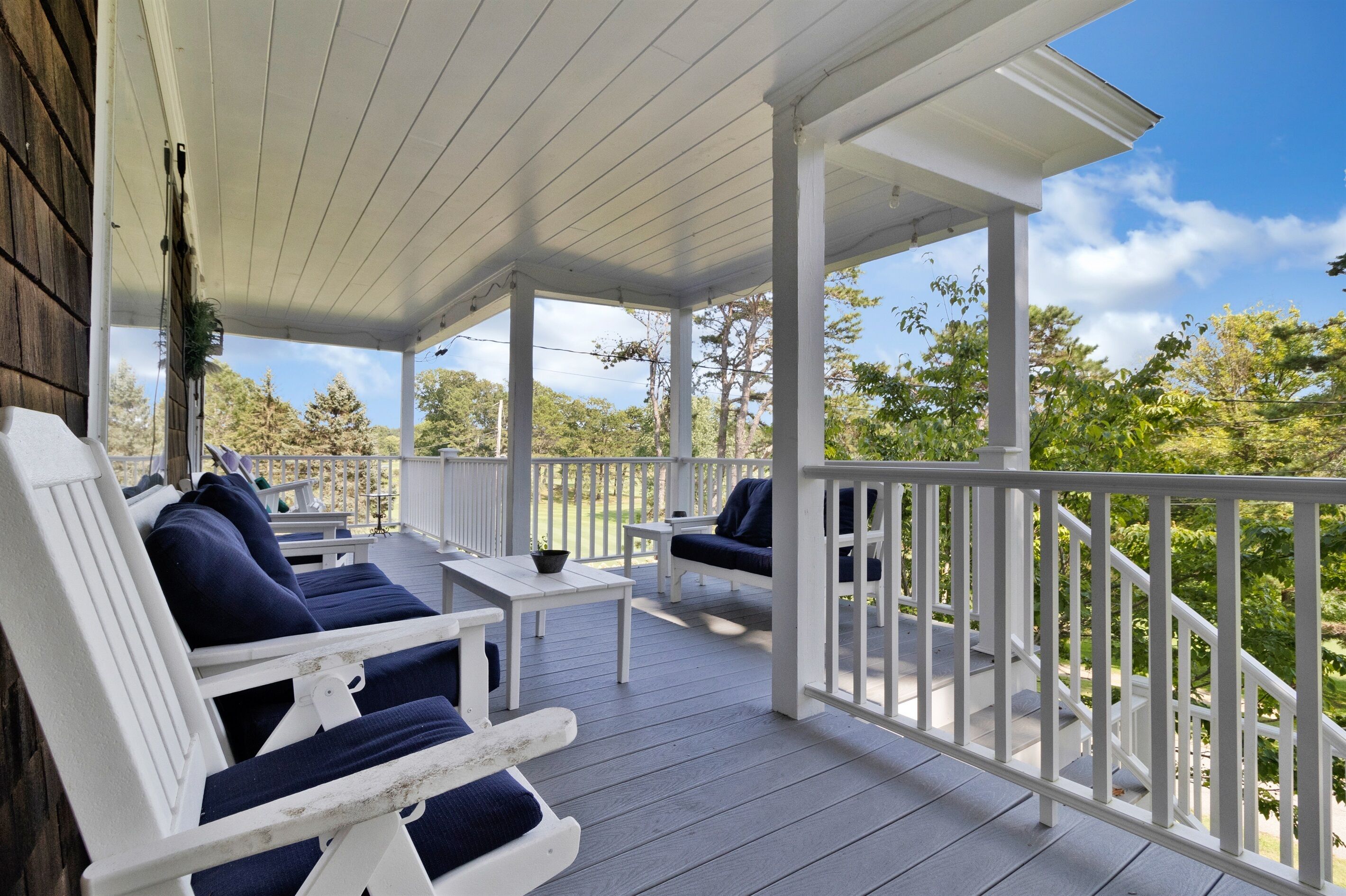 A covered porch with white railings, blue cushioned chairs, and a small table.