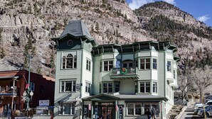 Un immeuble à plusieurs étages, doté d’une façade verdoyante, d’un balcon orné de blasons et d’une enseigne indiquant qu’il s’agit d’un hôtel.