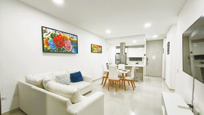 A modern living room with a white sofa, a dining area with a table and chairs, and a kitchen in the background. - Exclusive 3 Bedrooms - Samaria Beach Club (Santa Marta)