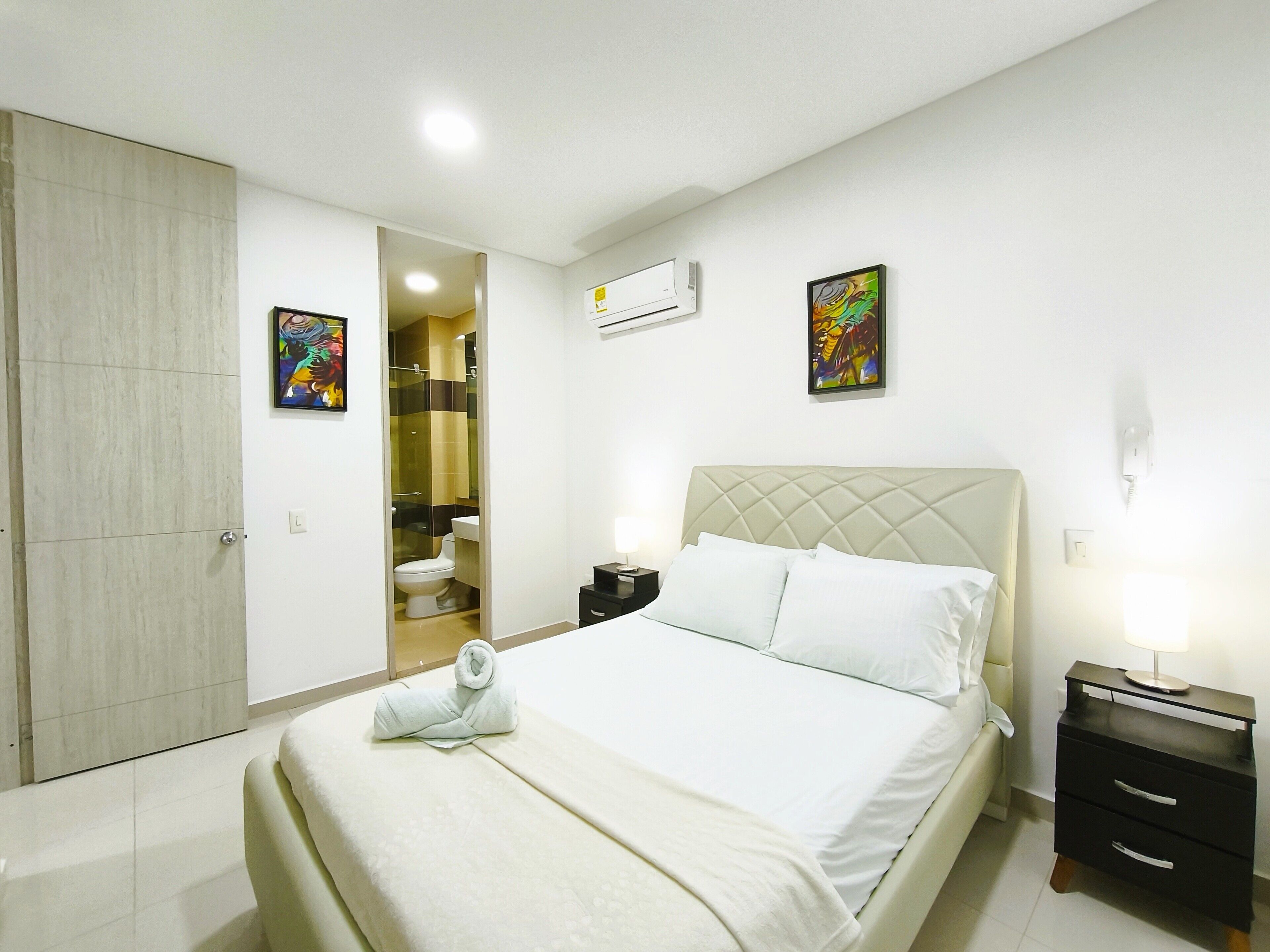 Une chambre d’hôtel avec un lit, une table de chevet, une lampe de chevet, une porte et une salle de bain visible à travers une porte ouverte.