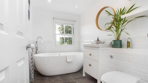 A modern bathroom with a freestanding bathtub, a toilet, and a vanity with a mirror and a potted plant. - Spacious and stylish flat in the vibrant neighbourhood of Mile End, East London! (Greater London)