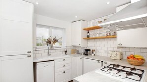 A modern kitchen with white cabinetry, a gas stove, a window with a view, and a fruit bowl on the counter. - Spacious and stylish flat in the vibrant neighbourhood of Mile End, East London! (Greater London)