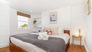 A bedroom with a bed, a window, a bedside table, and a wall-mounted picture. - Spacious and stylish flat in the vibrant neighbourhood of Mile End, East London! (Greater London)