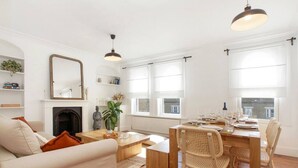 A well-lit living room with a fireplace, a dining area with a wooden table and chairs, and large windows allowing natural light. - Spacious and stylish flat in the vibrant neighbourhood of Mile End, East London! (Greater London)