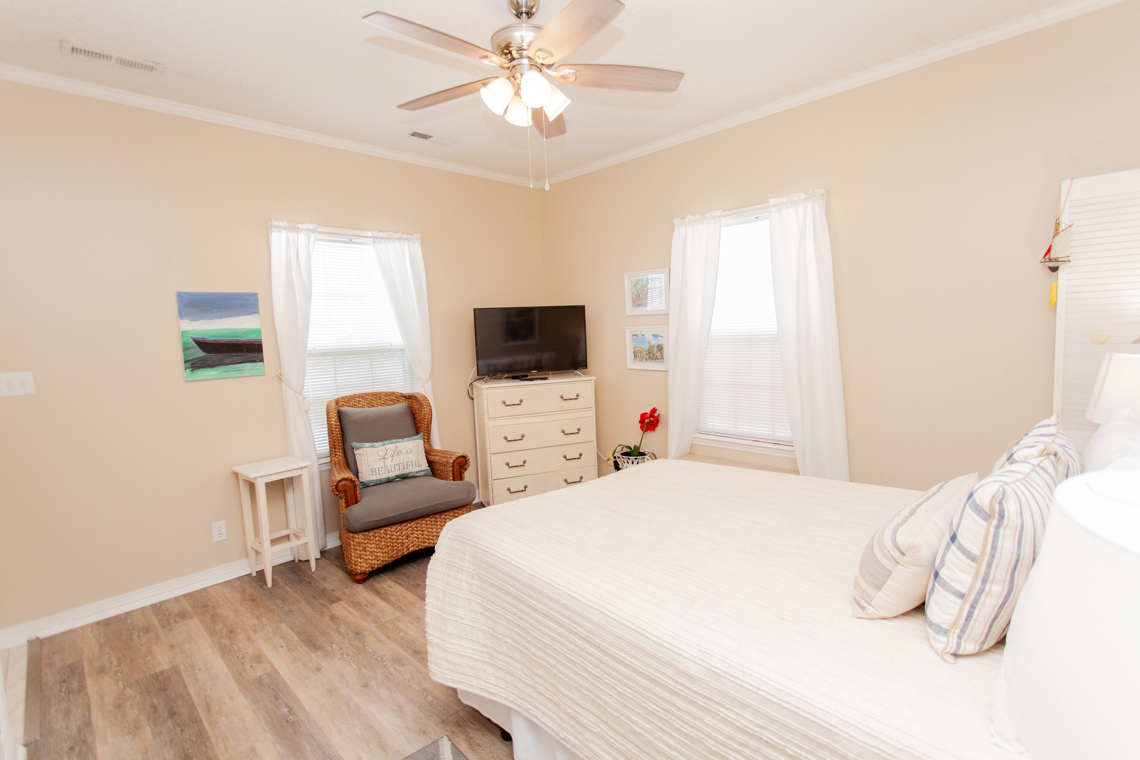 A bedroom with a bed, a television, a chair, a dresser, and a ceiling fan.
